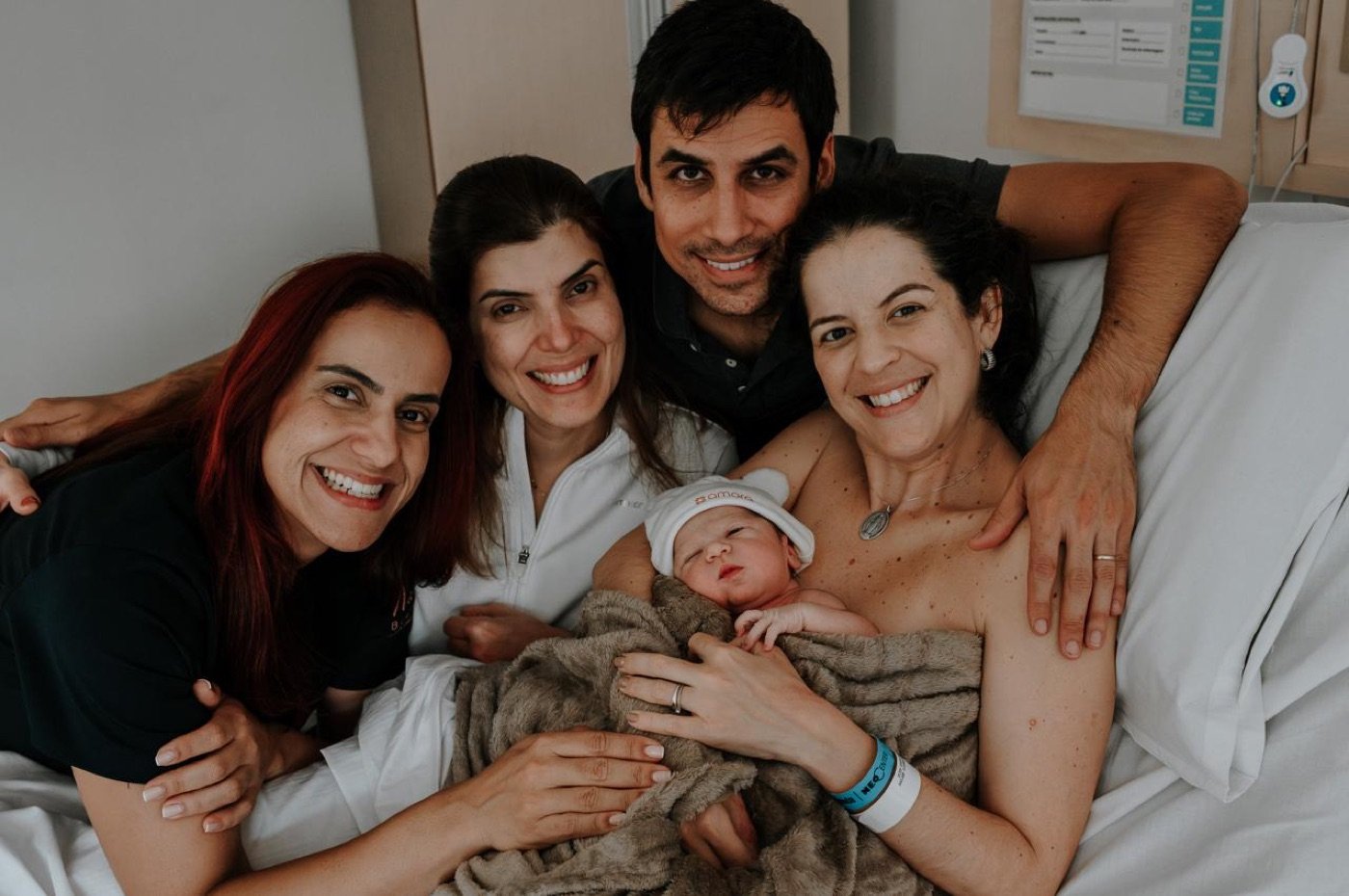 Dra. Marina Mariz e a equipe ao lado de uma família com o bebê recém-nascido no colo da mãe.