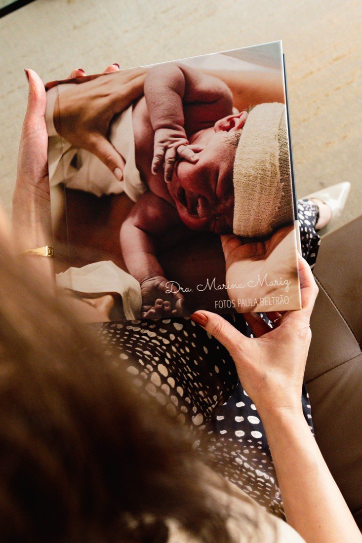 Mulher folheando um álbum de fotos da Dra. Marina Mariz com a imagem de um recém-nascido na capa.