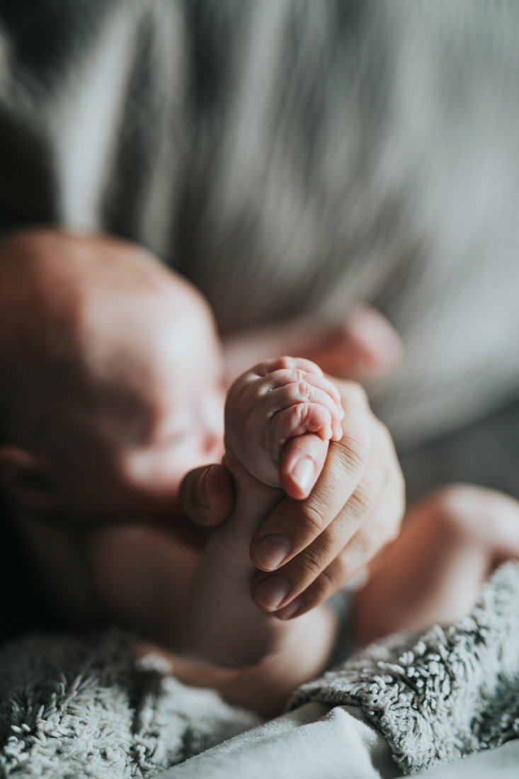 Mão de um recém-nascido adormecido segurando o dedo de sua mãe.